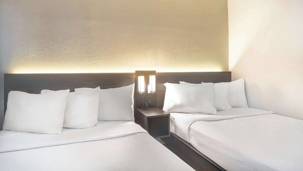 A hotel room with two beds, a nightstand with a lamp, and a textured wall. - Motel 6 Del Rio, TX (Del Rio)