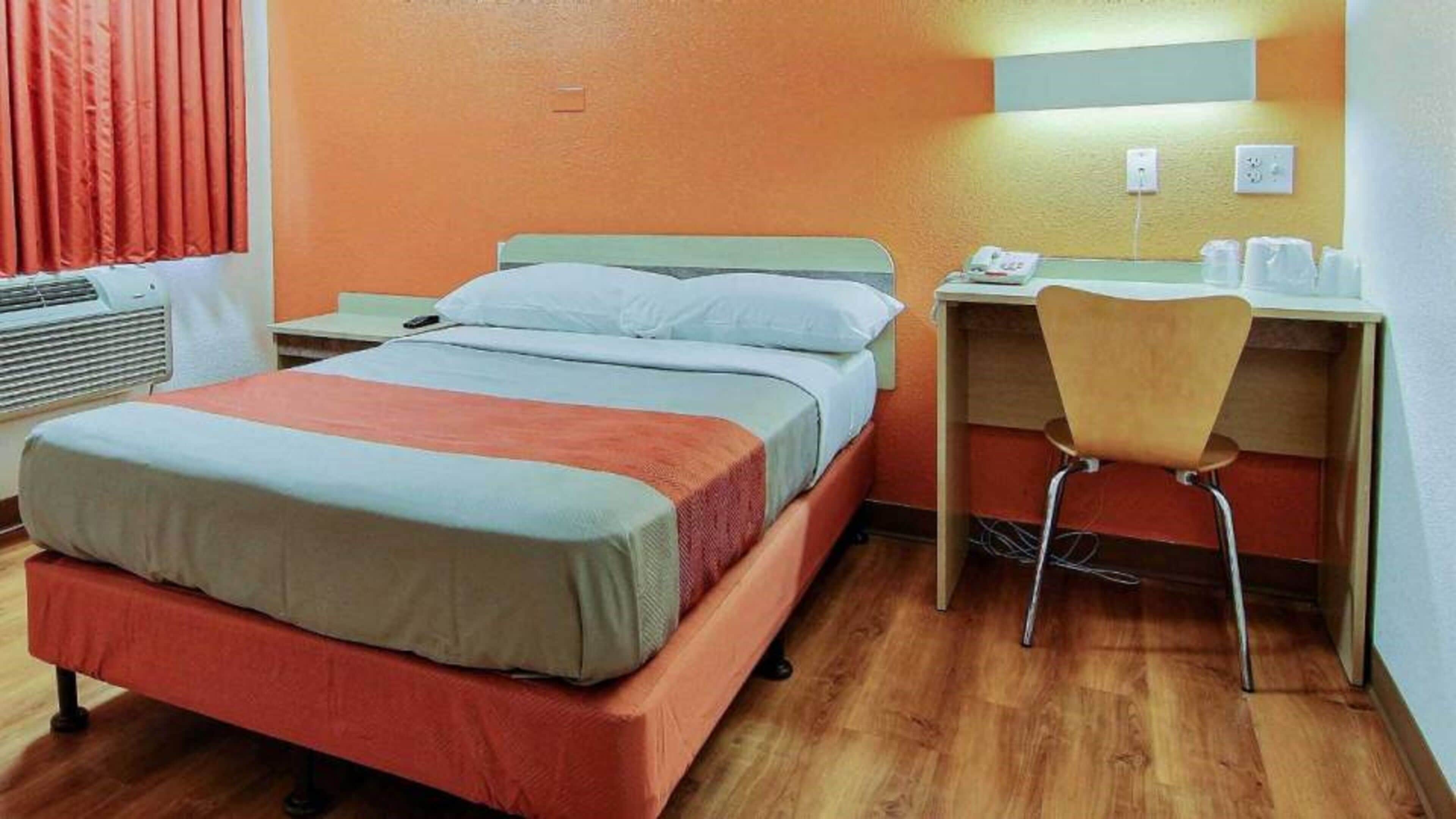 A hotel room with a bed, a desk with a chair, a telephone, and a window with curtains.