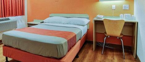 A hotel room with a bed, a desk with a chair, a telephone, and a window with curtains.
