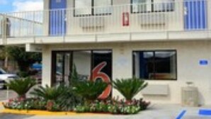 A building with a 'welcome' sign, a number '6' on the facade, and a small garden with plants in front.