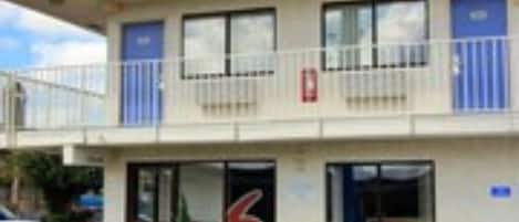 A building with a 'welcome' sign, a number '6' on the facade, and a small garden with plants in front.