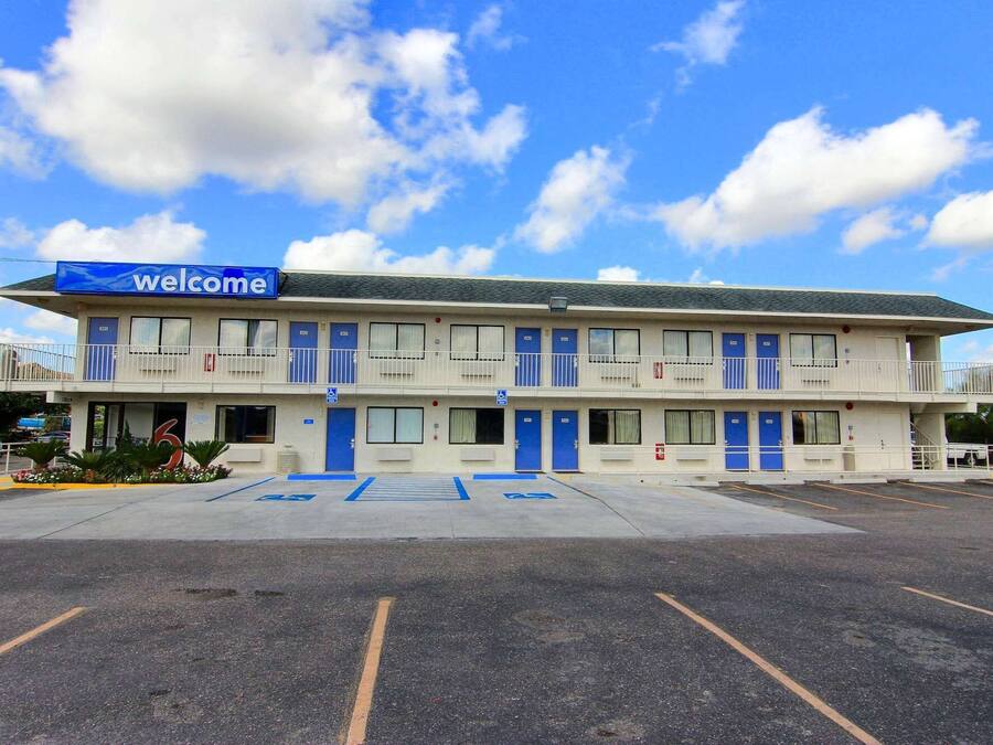 A motel with a 'Welcome' sign, multiple rooms, a parking lot, and handicap-accessible parking spaces.