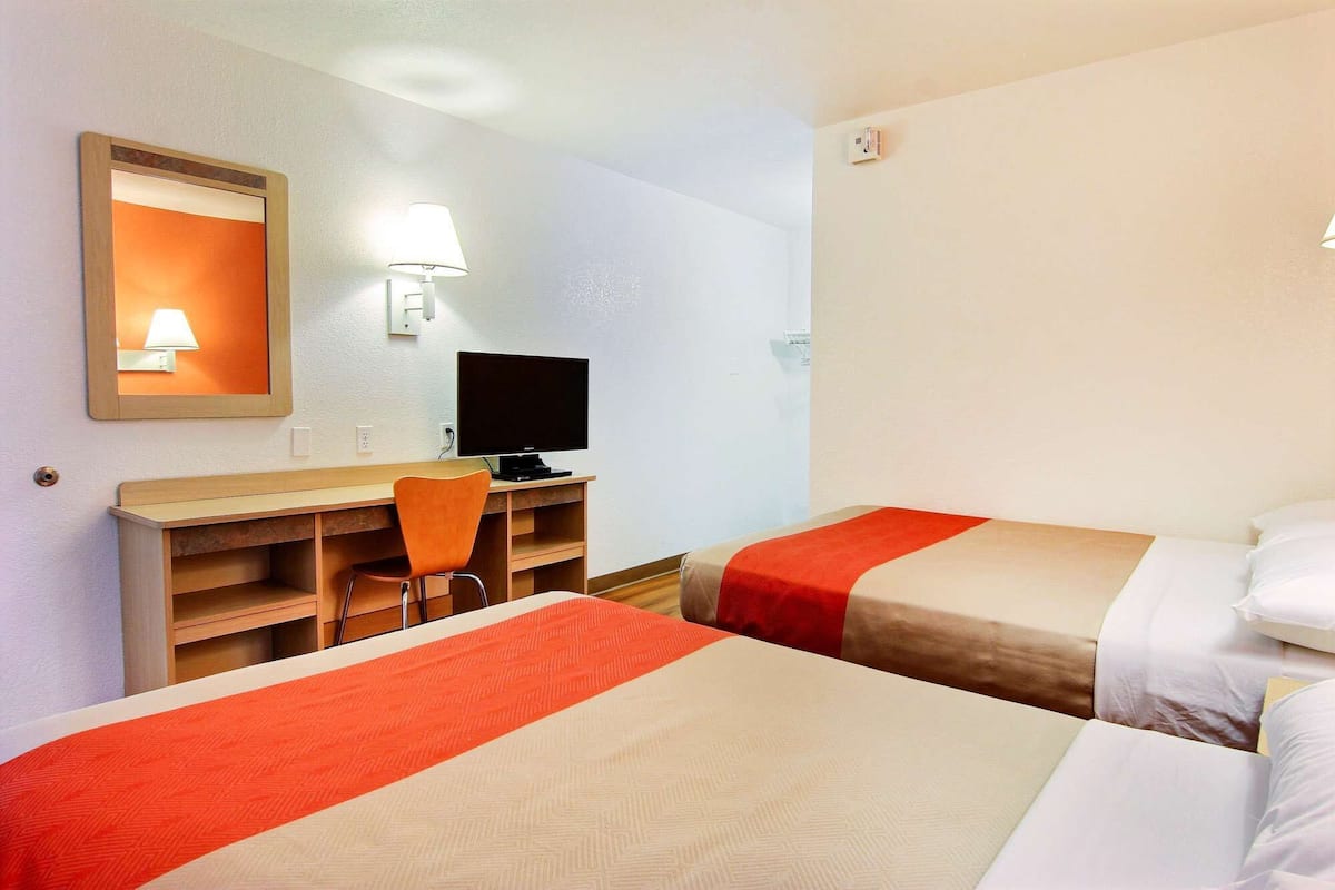 A hotel room with two beds, a desk with a computer, a chair, and a TV.