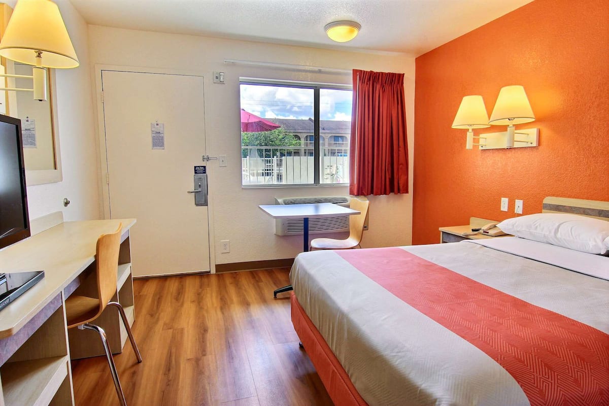 A hotel room with a bed, desk, chair, and a window with a view of the outside.