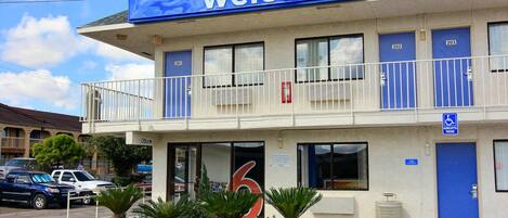 A motel with a 'Welcome' sign, numbered rooms, a balcony, and a handicapped parking sign.