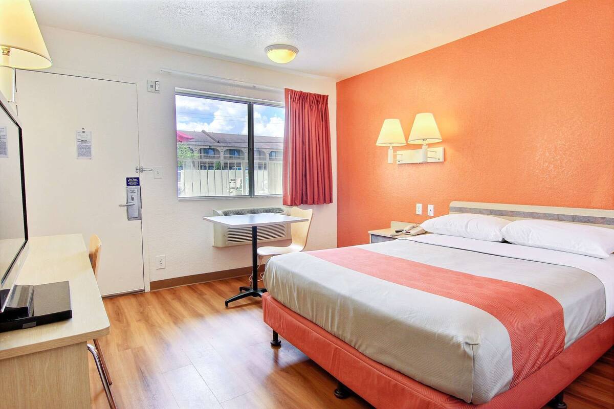 A hotel room with a bed, desk, chair, and a window with curtains.