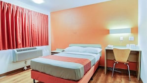 A hotel room with a bed, a desk, a chair, and a window with curtains.