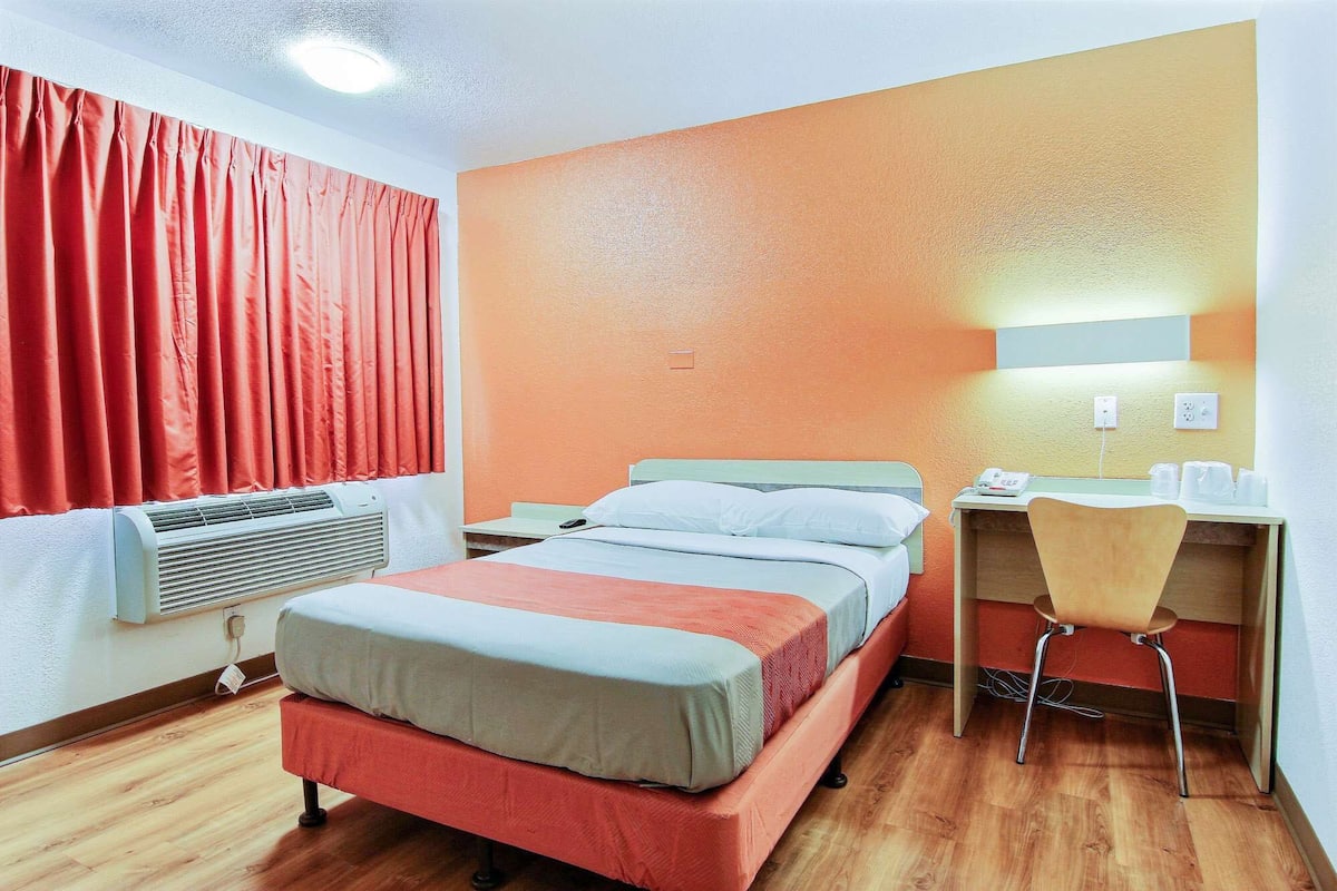 A hotel room with a bed, a desk, a chair, and a window with curtains.