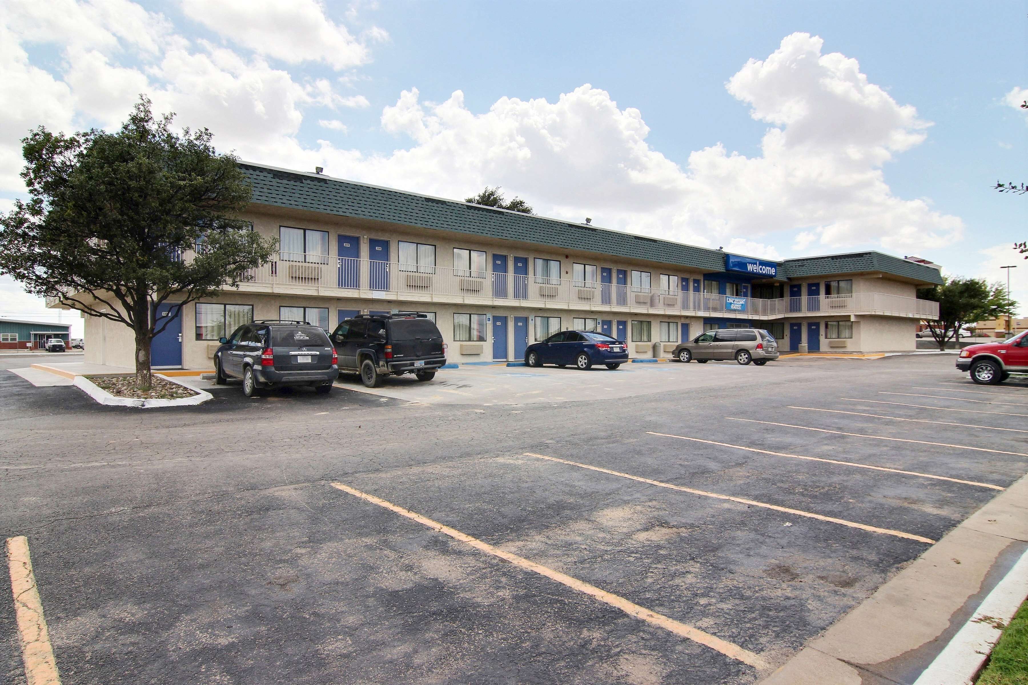 A motel with a parking lot, multiple cars parked, and a tree in the foreground.