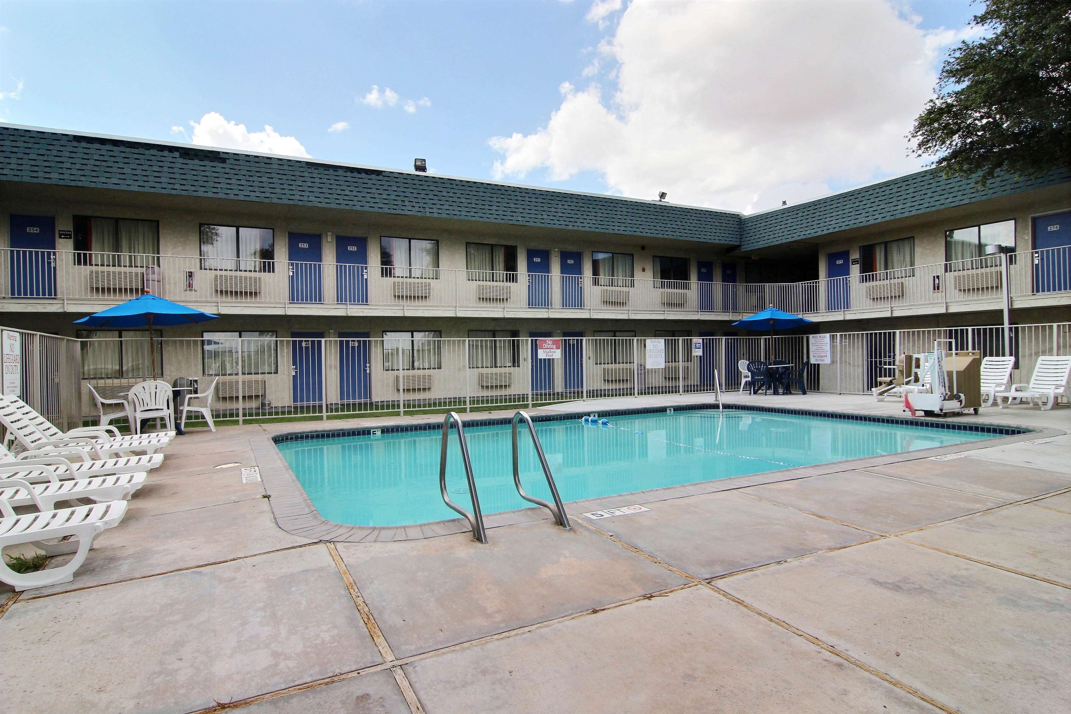 A motel with a swimming pool, outdoor seating, and a fenced balcony area.