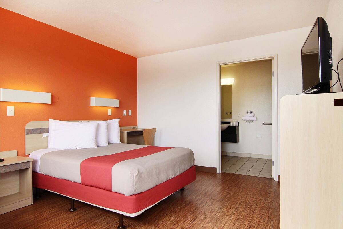 Una habitación de hotel con cama, mesitas de noche, televisión y baño visible a través de una puerta abierta.