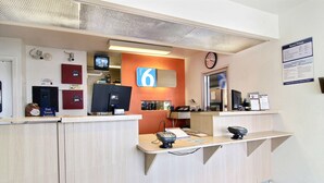 A hotel reception area with a reception desk, a clock, a TV, and a sign indicating room prices. - Motel 6 Fort Stockton, TX (Fort Stockton)