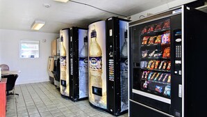 A row of vending machines with various snacks and drinks, a tiled floor, and a window with blinds. - Motel 6 Fort Stockton, TX (Fort Stockton)