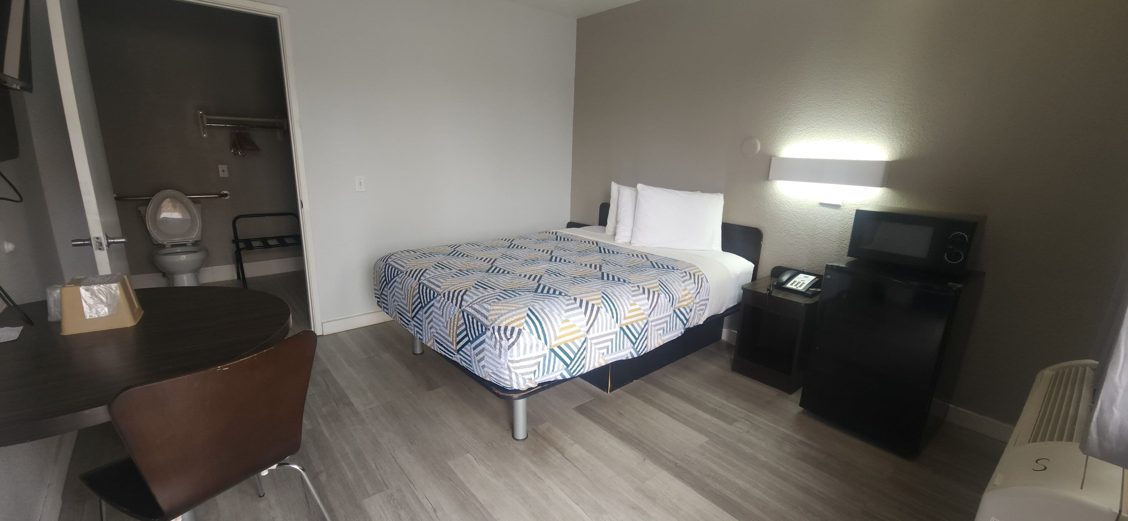 Ein Hotelzimmer mit Bett, Schreibtisch, Stuhl, Toilette, Fernseher und Heizung.