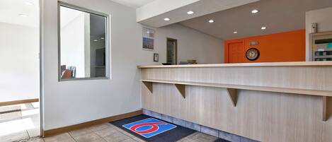 A hotel reception area with a wooden reception desk, a clock, and a door.