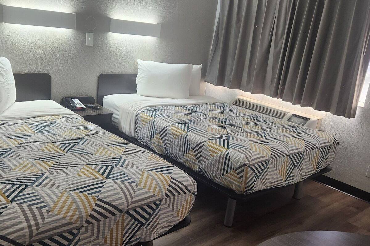 Habitación de hotel con dos camas, cada una con una colcha estampada, mesitas de noche con lámparas y una ventana con cortinas.