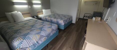 Habitación de hotel con dos camas, un escritorio, una silla y un televisor.