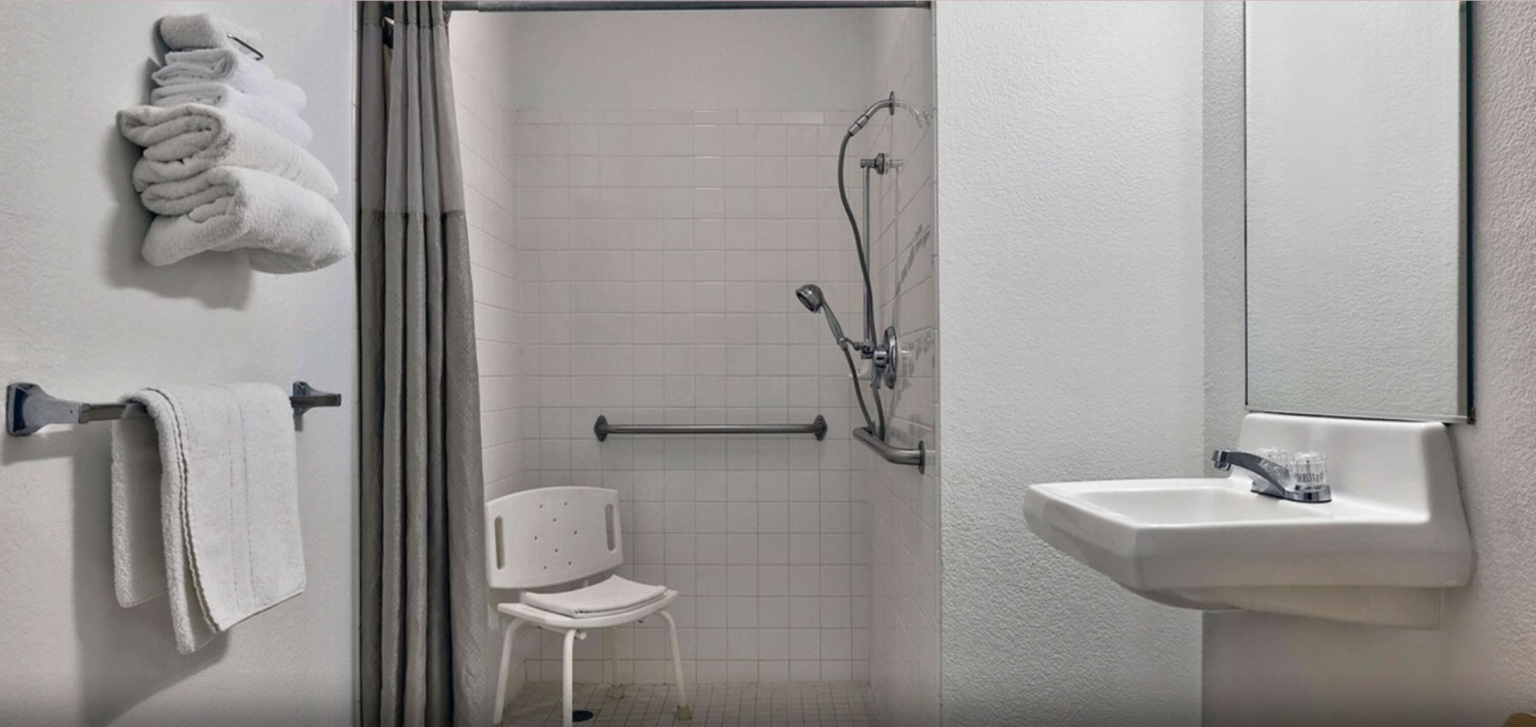 Un baño con ducha, lavamanos y una silla.