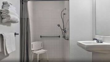 Un baño con ducha, lavamanos y una silla.