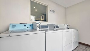 A laundry area with a Whirlpool washer and dryer, a mirror, and a sign indicating the model is not responsible for items left unattended. - Motel 6 Alamogordo, NM (Alamogordo)