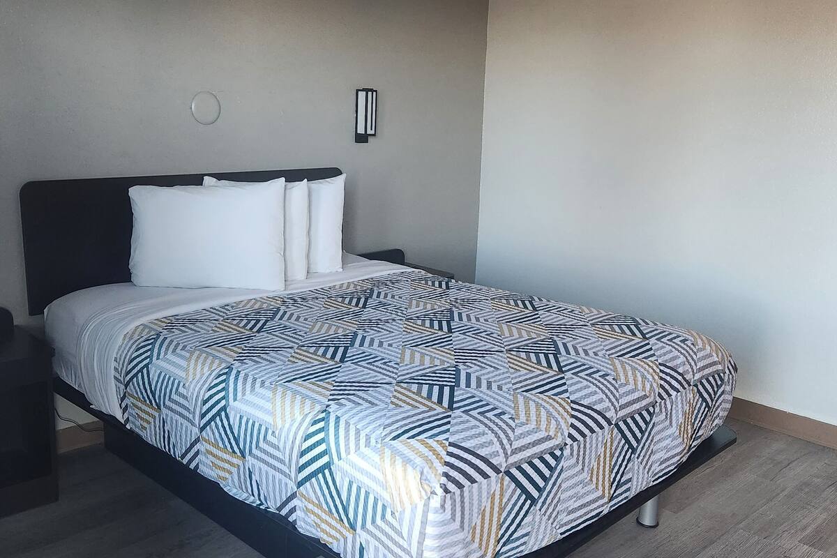 Una cama bien hecha con un edredón estampado, una mesita de noche con un teléfono y dos lámparas de pared.