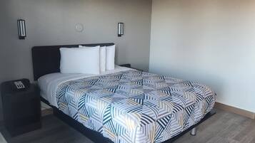A neatly made bed with a patterned bedspread, a bedside table with a phone, and two wall-mounted light fixtures.