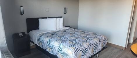 A neatly made bed with a patterned bedspread, a bedside table with a phone, and two wall-mounted light fixtures.