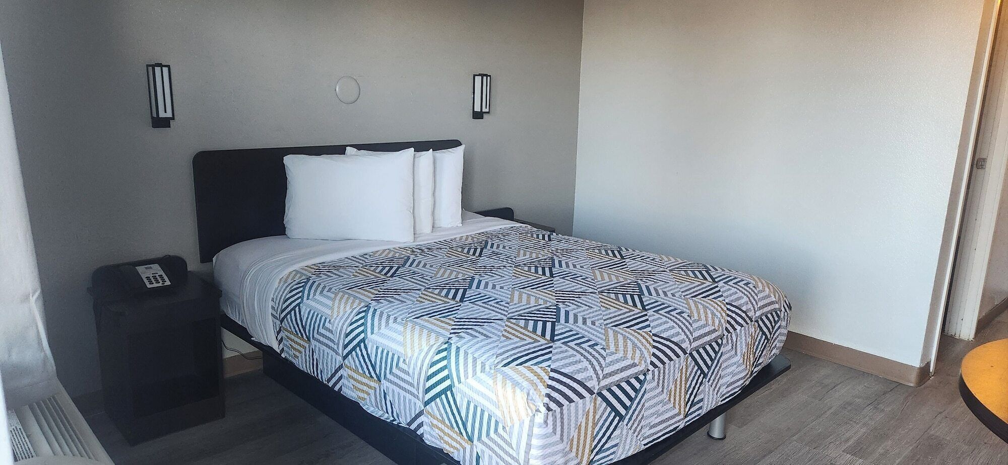 Una habitación de hotel con una cama, una mesita de noche con un teléfono y dos lámparas de pared.