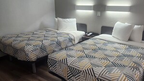 A hotel room with two beds, each with patterned bedding, a bedside table with a phone, and wall-mounted lighting. - Motel 6 Alamogordo, NM (Alamogordo)