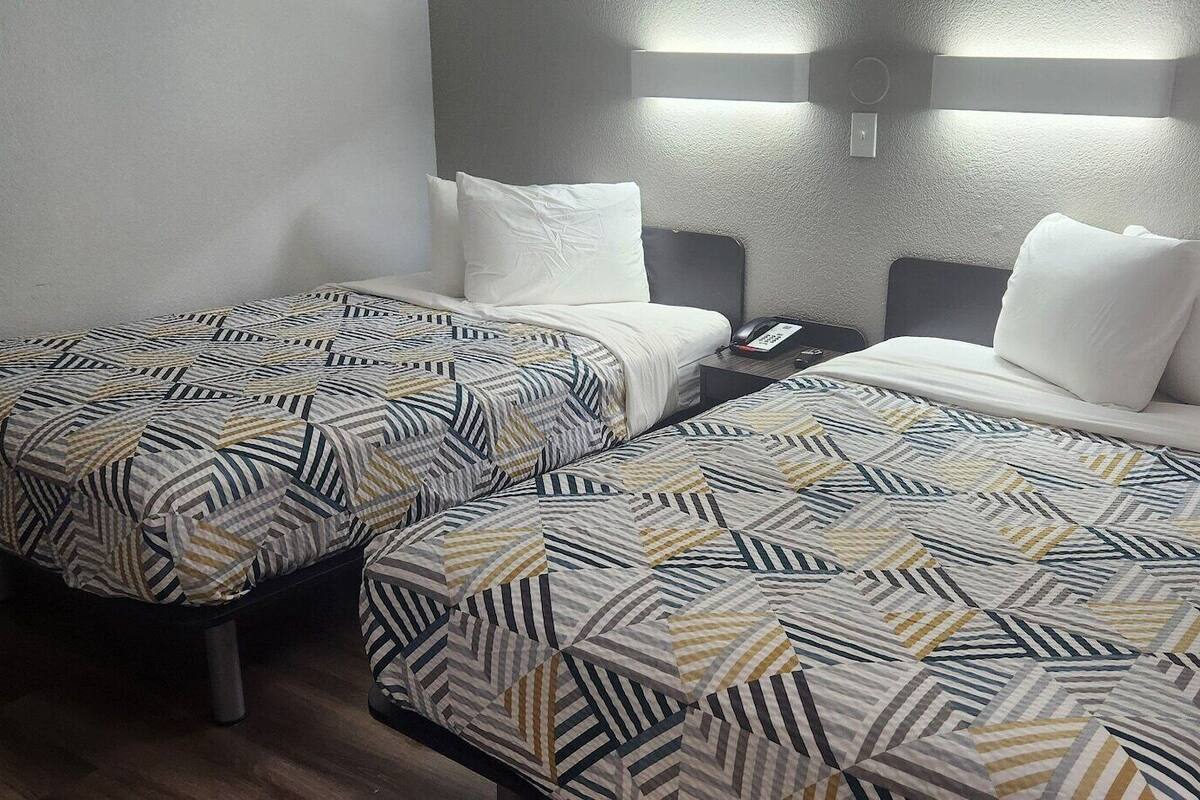 Habitación de hotel con dos camas, cada una con ropa de cama estampada, una mesita de noche con teléfono e iluminación montada en la pared.