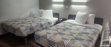 A hotel room with two beds, each with patterned bedding, a bedside table with a phone, and wall-mounted lighting.