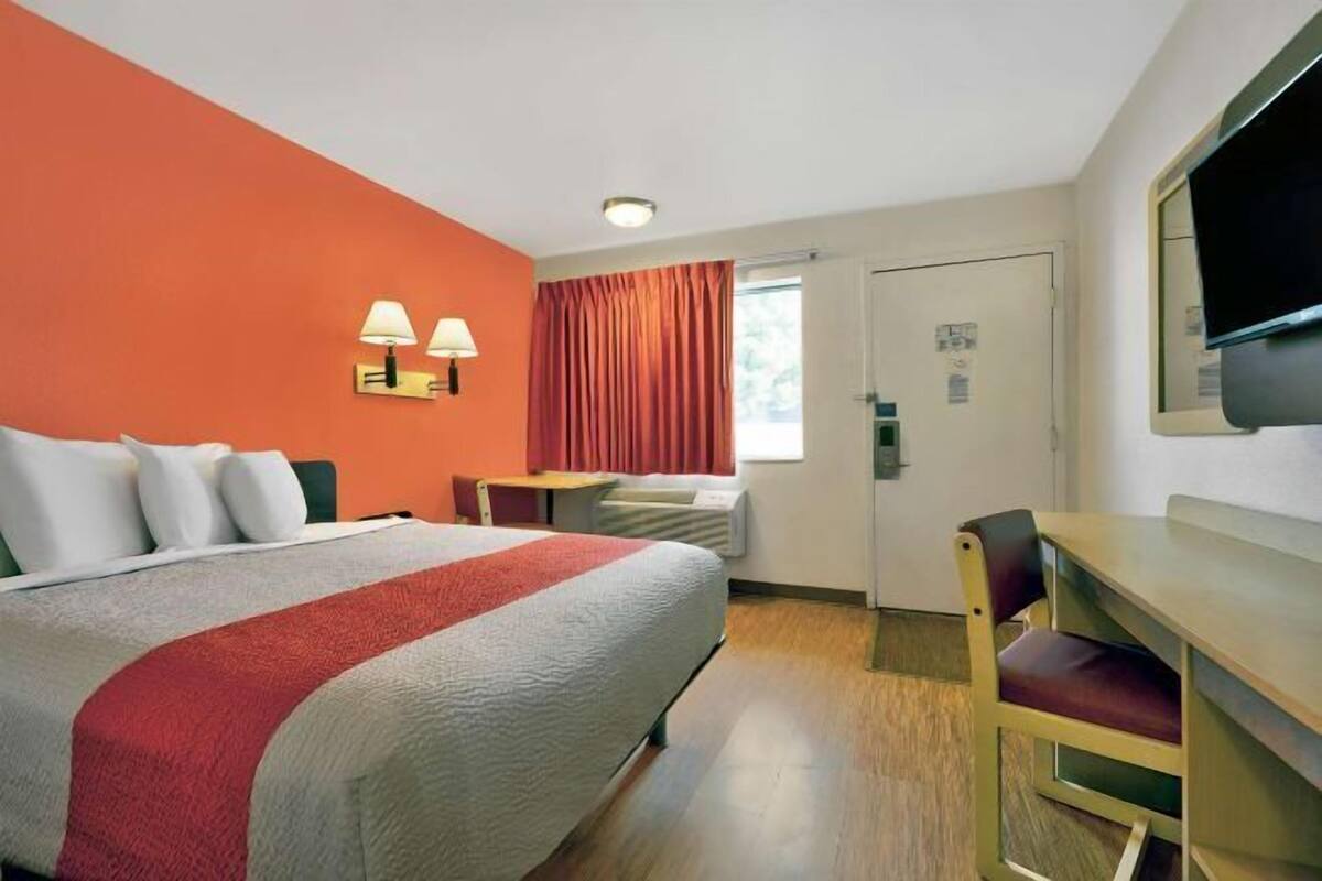 Habitación de hotel con cama, escritorio, silla, televisor y ventana con cortinas.