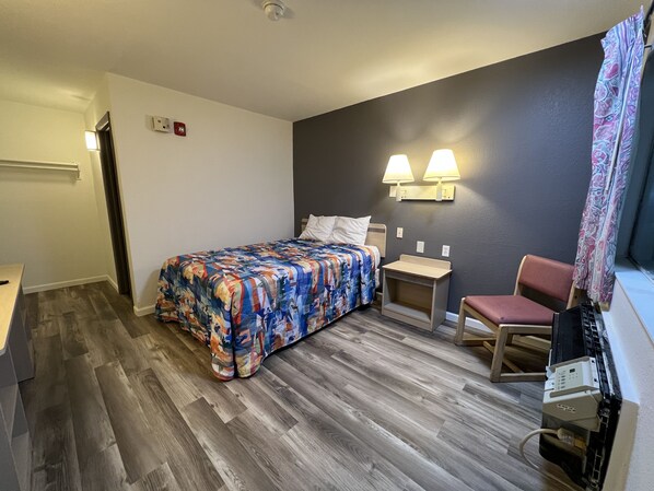 A hotel room with a bed, bedside tables, a chair, and a desk.