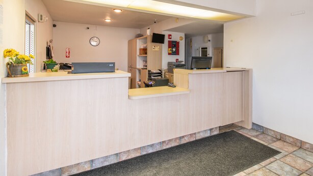 Et receptionsområde med en træreception, et ur på væggen og en lille plante på disken.