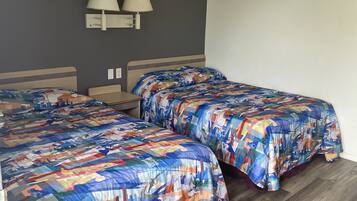 A room with two beds, each with a colorful quilt, a wall-mounted lamp, and a wooden floor.