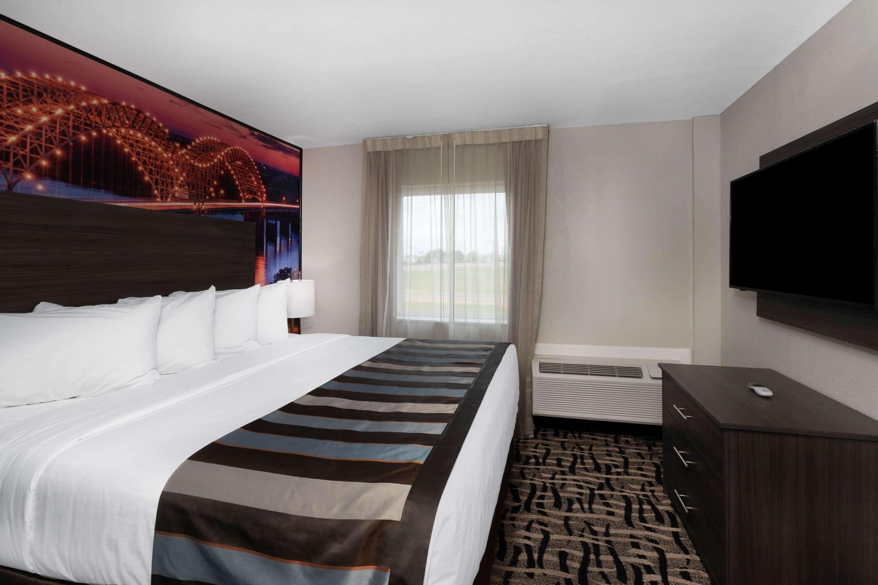 Habitación de hotel con una cama grande, un televisor de pantalla plana, un escritorio con una computadora y una ventana con cortinas.