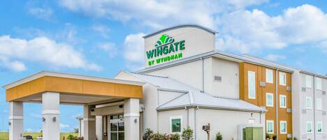 A Wingate by Wyndham hotel with a covered entrance, multiple floors, and a clear sky.