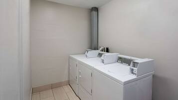 A laundry room with a front-loading washer and dryer, a ventilation hood, and a tiled floor.