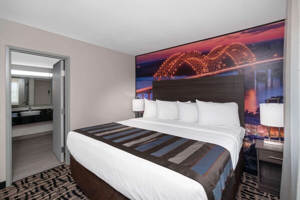 Habitación de hotel con una cama grande, una mesita de noche, una lámpara, un televisor montado en la pared y un baño visible a través de una puerta abierta.