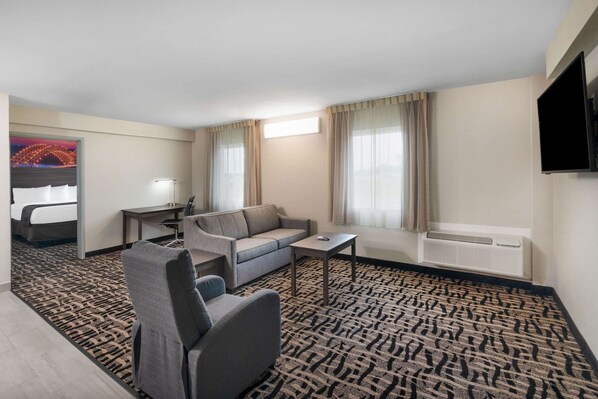 Habitación de hotel con sofá, sillón, mesita y televisor instalado en la pared.