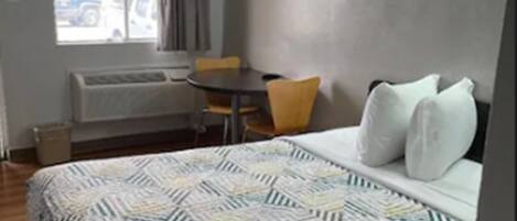Una habitación de hotel con una cama, una ventana con cortinas, una mesa con sillas y un radiador.