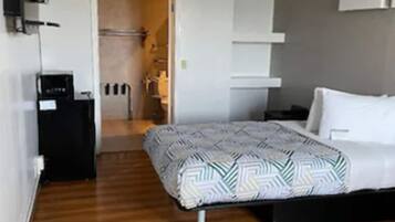 Un dormitorio moderno con suelo de madera, una cama con ropa de cama estampada, una mesita de noche, un televisor montado en la pared y una puerta que da a un baño.
