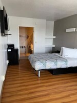 Un dormitorio moderno con suelo de madera, una cama con ropa de cama estampada, una mesita de noche, un televisor montado en la pared y una puerta que da a un baño.