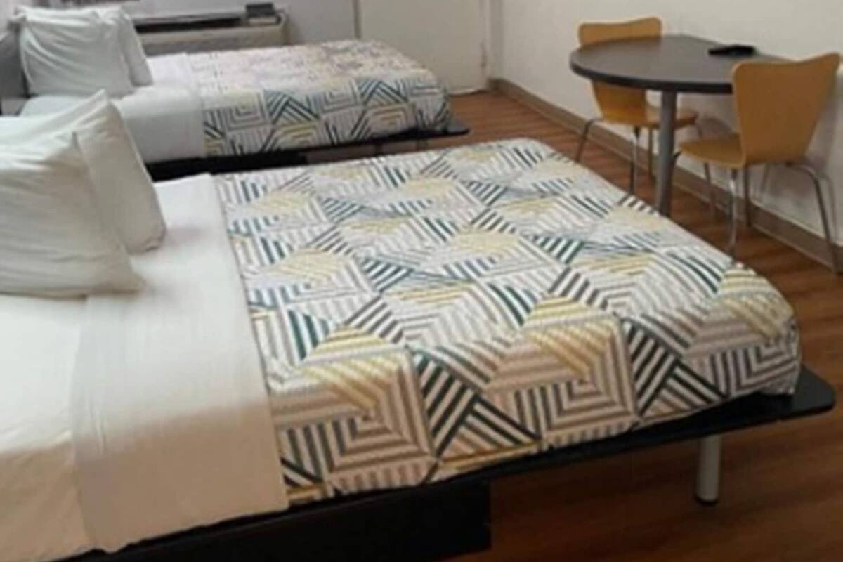 Hotellihuone, jossa on kaksi sänkyä, pieni pöytä, tuoleja, televisio ja ikkuna, jossa on verhot.