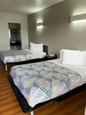 Habitación de hotel con dos camas, cada una con ropa de cama estampada, una mesita de noche con teléfono y una lámpara fijada a la pared.