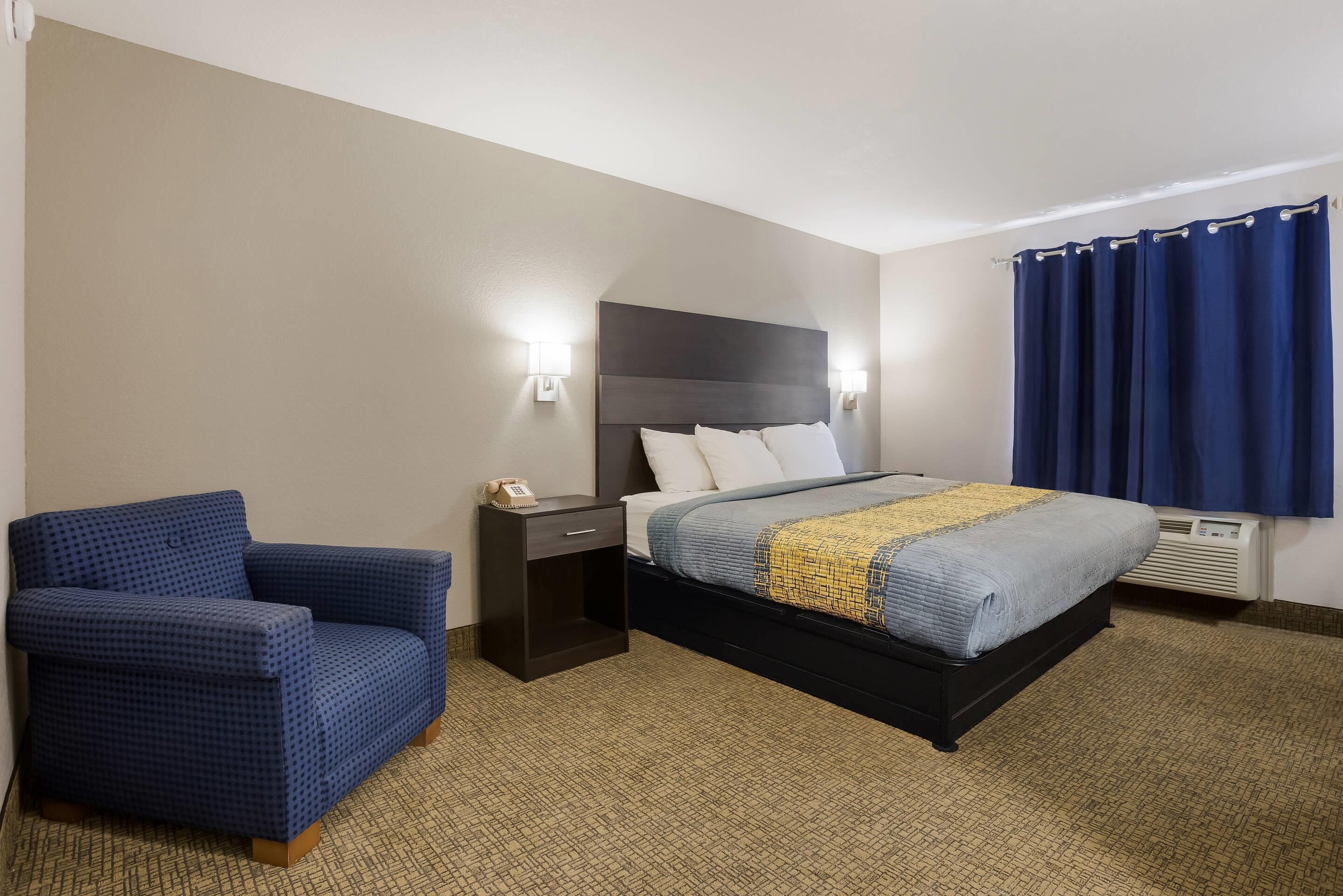 Une chambre d’hôtel avec un lit, une chaise, une table de chevet et une lampe fixée au mur.