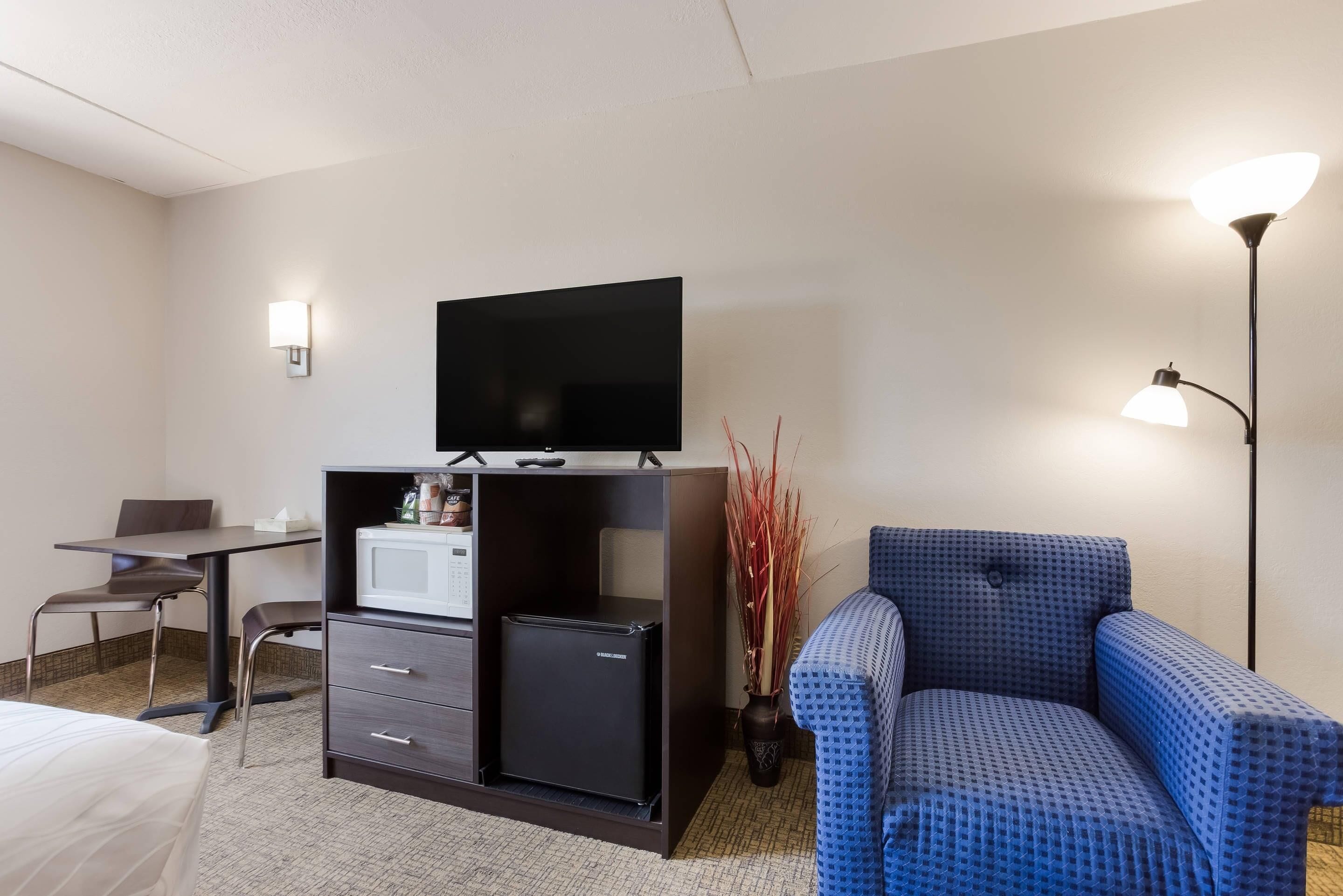 A hotel room with a bed, a desk with a chair, a television on a cabinet, a sofa, and a lamp.