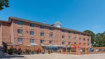A multi-story brick building with a central glass entrance, outdoor seating area, and a covered walkway.