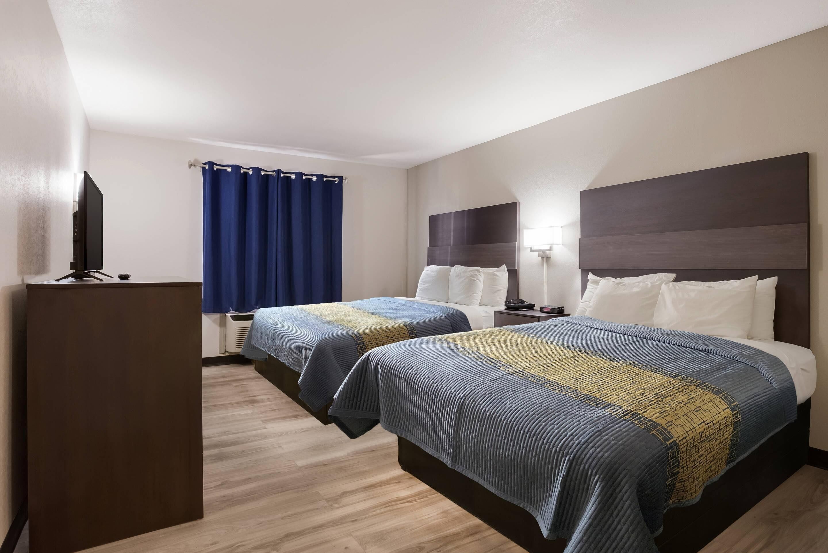 Quarto de hotel com duas camas, televisão, escrivaninha e janela com cortinas.