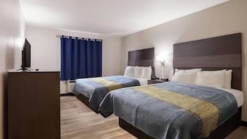 Quarto de hotel com duas camas, televisão, escrivaninha e janela com cortinas.